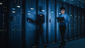 An IT professional walks by servers in a darkly lit room.
